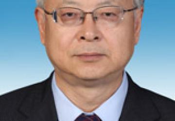 Head-to-shoulders close up of Sen Pang. He wears a dark suit, glasses and stands in front of a gradient blue background.