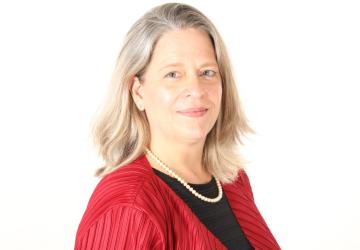 Una mujer, con camisa negra y chaqueta roja, mira directamente a la cámara.