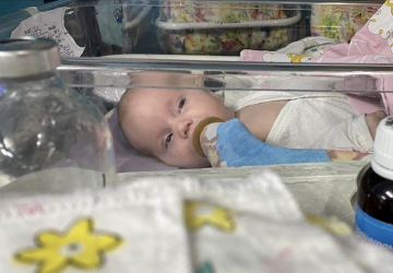 A baby lays in a plastic crib with an oxygen tube in their mouth. 