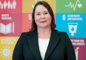 امرأة تقف أمام لافتة عليها شعارات أهداف التنمية المستدامة.