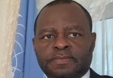 رجل يقف بجانب علم الأمم المتحدة الأزرق وينظر للكاميرا.