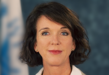 تقف المنسقة المقيمة المعينة حديثًا في كوسوفو أمام علم للأمم المتحدة.