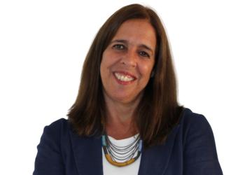 A woman in a blue blazer crosses her hands and smiles for the camera.