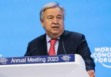 The head of the UN speaks at a podium, with a light blue World Economic Forum banner behind him. 