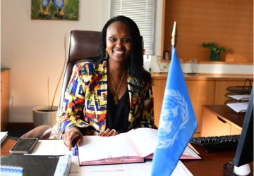 Woman in a colourful shirt sitting at a desk with a UN flag in the foreground
