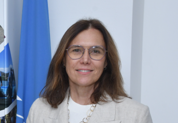 Woman in a white suit with glasses standing in front of a united nations blue coloured flag
