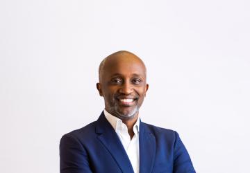 A man in a blue suit and white shirt with his arms crossed, against a white background