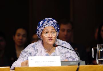A woman in a purple dress and headscarf speaks into a microphone
