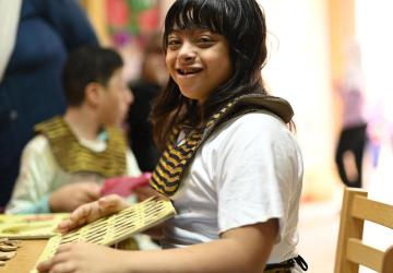 A picture of a girl in a white shirt, playing with a wooden card in a school classroom