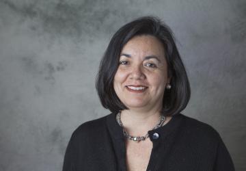 A woman in a black shirt and silver necklace with a bob hairstyle smiles into the camera.