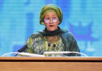 A woman in a green dress and headscarf speaks at a podium