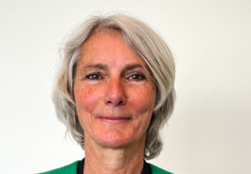 A woman in a green shirt stands in front of a white wall.
