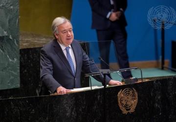 A man inn a dark grey suit and blue tie, the UN Secretary-General, speaks from a podium at the UN building