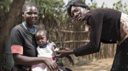 الأم تجلس مع ابنتها الصغيرة بينما تضع المرأة رباطًا حول ذراع الطفلة.