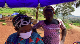 Deux femmes, dont l'une porte un masque de protection, se tiennent sous un parasol bleu.