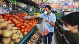 Abdou, un refugiado yemení en Ammán, hace mercado en una frutería tras la reapertura de pequeñas empresas. Lleva una mascarilla protectora y guantes. En primer plano de la imagen, un niño, también con mascarilla, lo ve meter tomates en una bolsa de plástico.