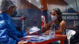 Un miembro del personal de la OIM que lleva una mascarilla y equipo de protección personal está sentado frente a una mesa. Del otro lado de la mesa, una mujer que también lleva una mascarilla protectora recibe el documento que la primera persona descrita le entrega. La mujer levanta el pulgar en forma afirmativa, transmitiendo que todo está en orden.