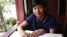 Thaw Lay, un estudiante de Yangon, Myanmar, hace sus deberes en casa. Está sentado a una mesa, cerca de una ventana detrás de la cual se adivina un jardín. Sonríe mientras mira a la cámara.