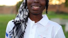 Foto de la poetiza Hama Daouda Fatouma vistiendo un polo blanco, con el logo de la Iniciativa Spotlight, y sonriendo para la cámara.