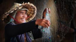 La photo intitulée "Happy work" montre une femme portant un chapeau traditionnel en forme de cône en train de sécher un filet de pêche. La femme arbore un grand sourire.