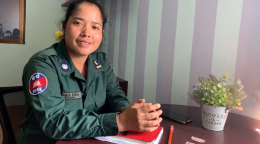 La agente de policía Kong Ravin, sonríe a la cámara mientras está sentada con su uniforme y las manos juntas sobre una mesa.