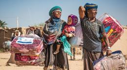 A displaced family in Marib, Yemen, carries a winter aid package back to their shelter.