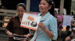 A woman in a blue shirt holds up a sign while another woman in a red shirt looks down at three other signs in her hands. 