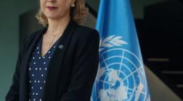 La nouvelle Coordonnatrice résidente des Nations Unies au Brésil, Silvia Rucks, se tient debout devant le drapeau de l’ONU, face caméra.
