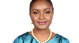 Una mujer con un vestido azul claro y el pelo recogido en un moño sonríe a la cámara.