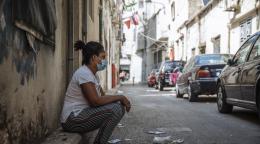 Una mujer con una mascarilla azul está sentada a un lado de la carretera.