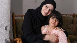 Ghada sonríe alegremente a la cámara mientras abraza con orgullo a su hija menor, que también sonríe a la cámara.