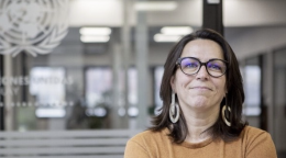 Una mujer con una camisa naranja y gafas negras se encuentra en una oficina de las Naciones Unidas con los brazos cruzados.