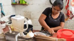 Une femme vêtue d'un haut noir prépare un repas dans une cuisine.