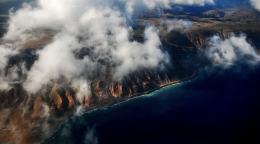 An areal shot of a coastline with clouds in the sky.