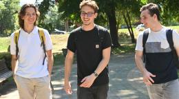 Three young men, Teo (left), Orhan (middle) and Boris (right), walk happily together in a park. 