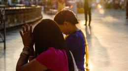 Two women praying outside while the sun is setting in the background. 