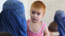 En primer plano aparece una madre con tocado y rostro mientras sostiene a su bebé, y en segundo plano se encuentra otra madre y su pequeño.