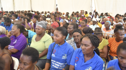 A large group of women sit together in a large tent. 