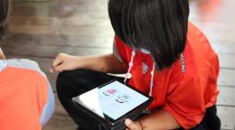 Two children sit near each other one the floor. Once child looks at a tablet. 