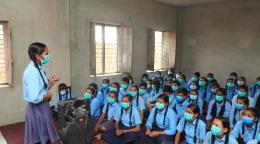 A girl stands in front of a class full of students in their school uniforms. 