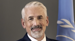A man with his arms crossed stands in front of the United Nations flag.