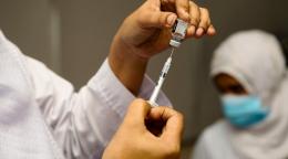 عامل صحي يجهز الحقنة ويقف خلفه عامل صحي آخر يضع كمامة.