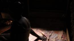 A silhouette of a girl sitting on a bed with one arm extended. 