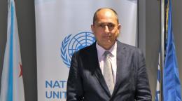 A man stands in front of two flags, posing for a photo.
