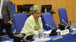 امرأة ترتدي شالًا أصفر على كرسي أزرق تتحدث في ميكروفون في اجتماع للأمم المتحدة.