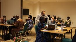 Groups of 4 people sit behind computers, dotted around a room, in what appears to be a hands-on training session.