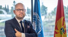 رجل يرتدي بدلة يقف بجانب علمي الأمم المتحدة والجبل الأسود.