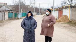 Две женщины в зимних пальто разговаривают на улице. 