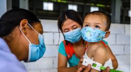 ممرضة تقوم بتلقيح طفل صغير بينما تمسكه أمه.