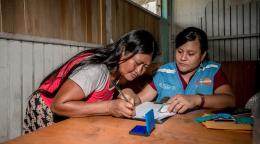 Dos mujeres sentadas a una mesa y concentradas en lo que están escribiendo.